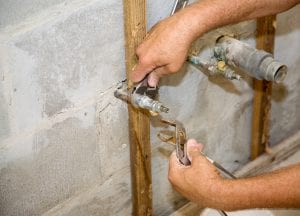Plumbers hands using a wrench and pliers to loosen a pipe. 