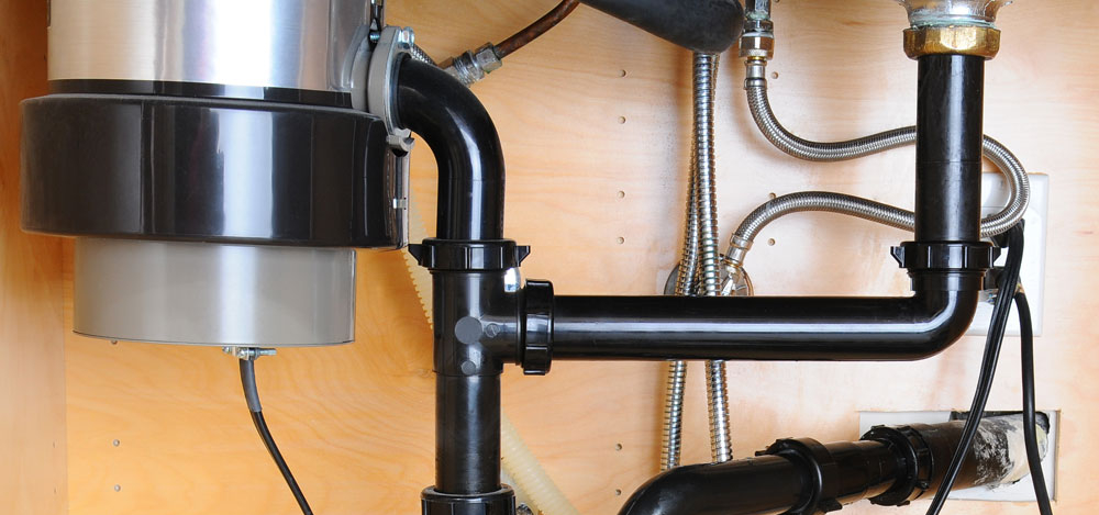 A look at a garbage disposal and associated plumbing under the kitchen sink to illustrate how to unclog a garbage disposal.
