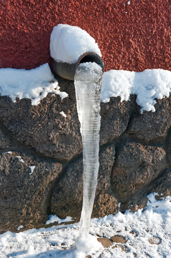 An icicle hangs from an outdoor pipe to help illustrate how to prevent frozen pipes.